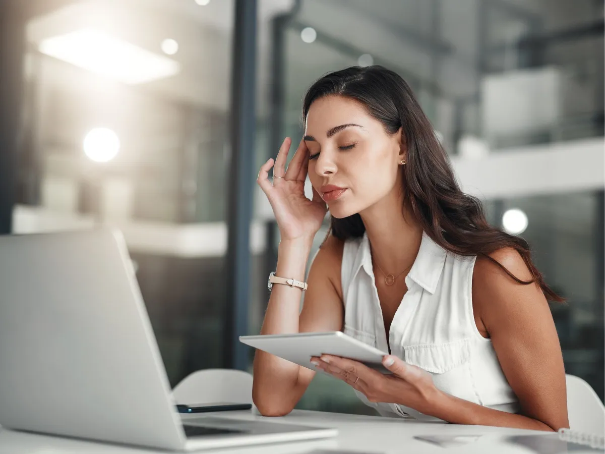 Woman at work with a laptop and tablet rubbing her head