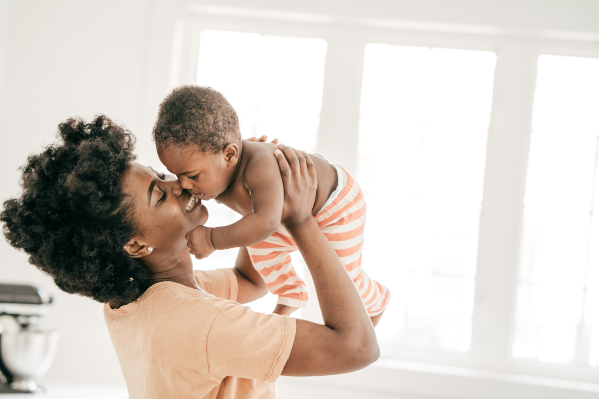 Smiling mom raising her baby in the air and snuggling his face